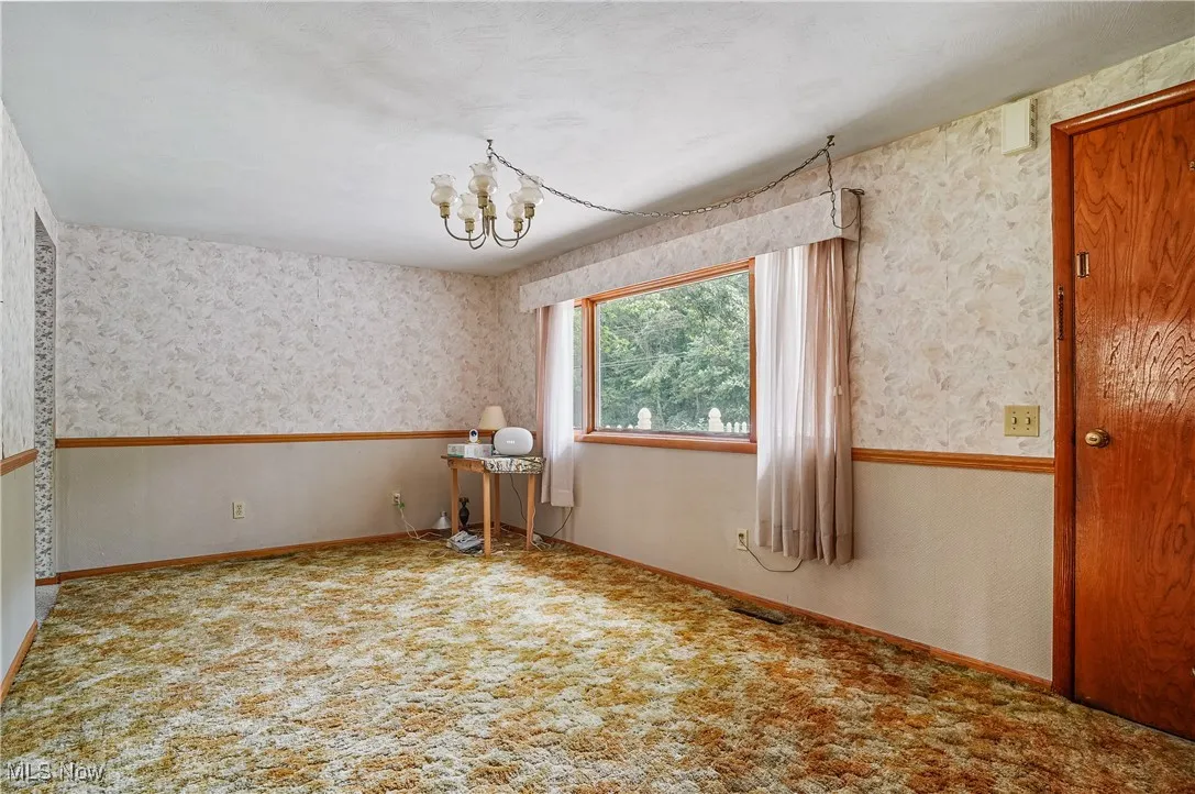 Unfurnished room with a chandelier, wallpapered walls, and carpet
