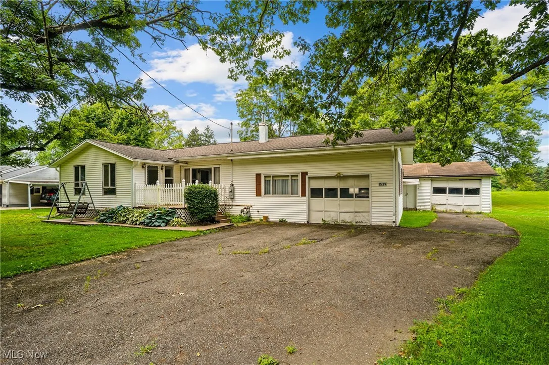 Single story home featuring a garage, a chimney, asphalt driveway, and a front lawn