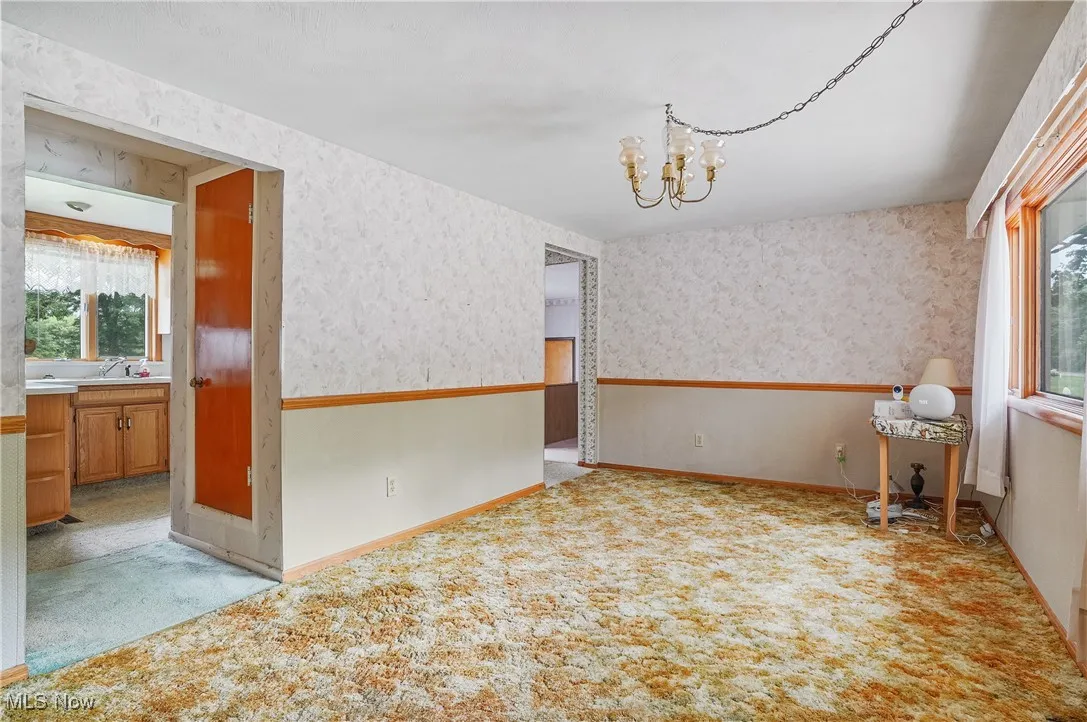 Unfurnished room with a chandelier, wallpapered walls, and light carpet