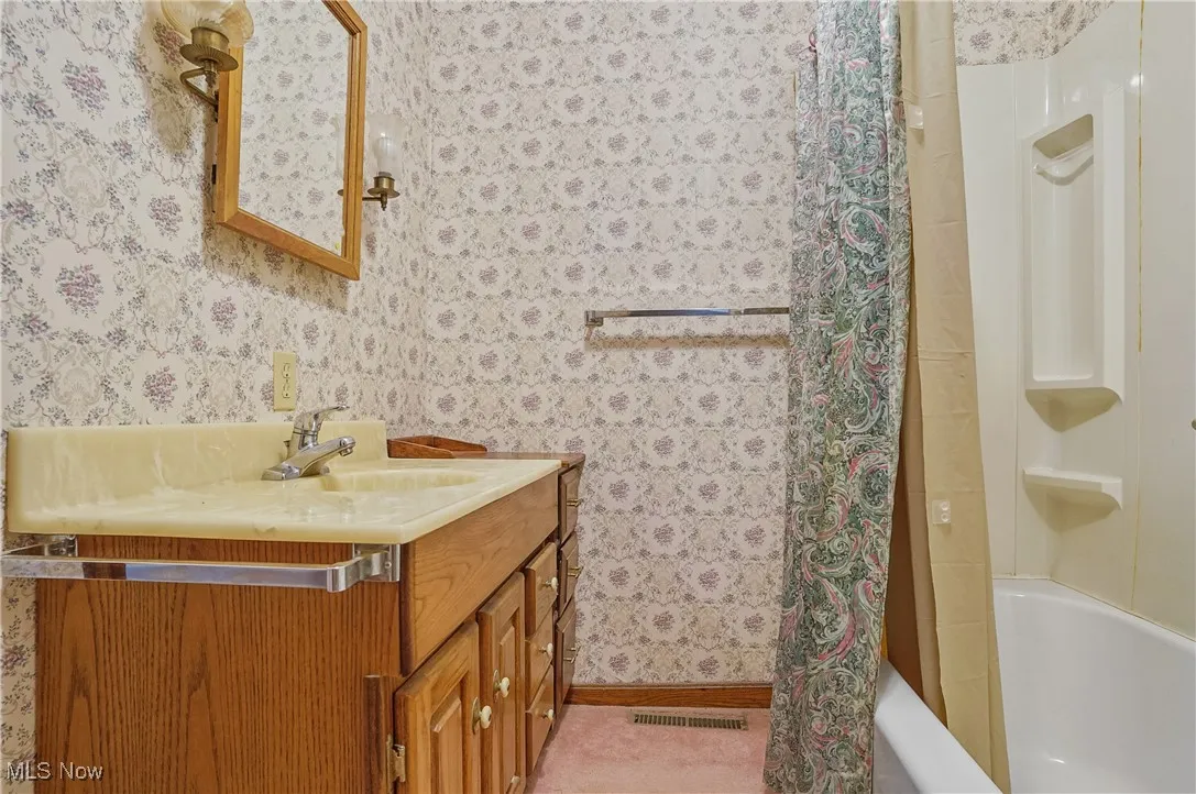 Full bath with vanity, wallpapered walls, and shower / tub combo