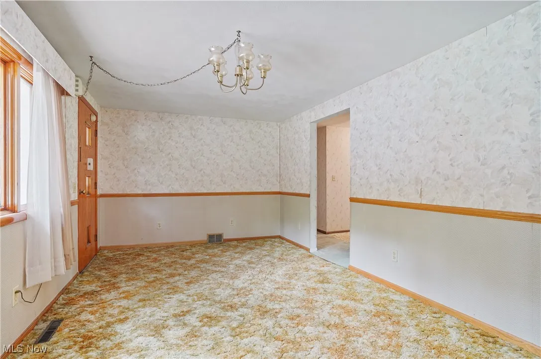 Empty room with a chandelier, wallpapered walls, and carpet floors