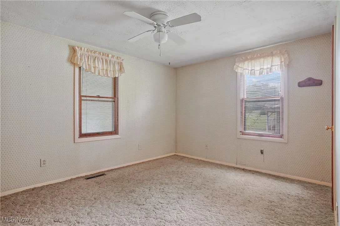 Carpeted empty room with a textured ceiling, a ceiling fan, and wallpapered walls
