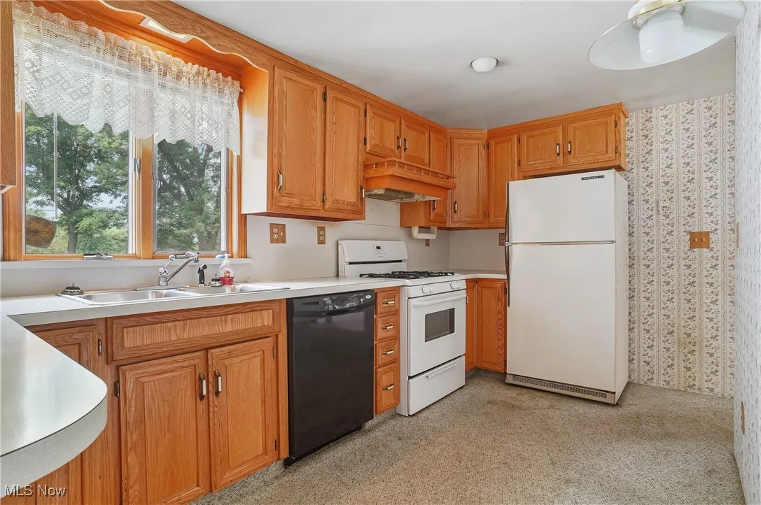 Kitchen featuring white appliances, premium range hood, light carpet, light countertops, and wallpapered walls