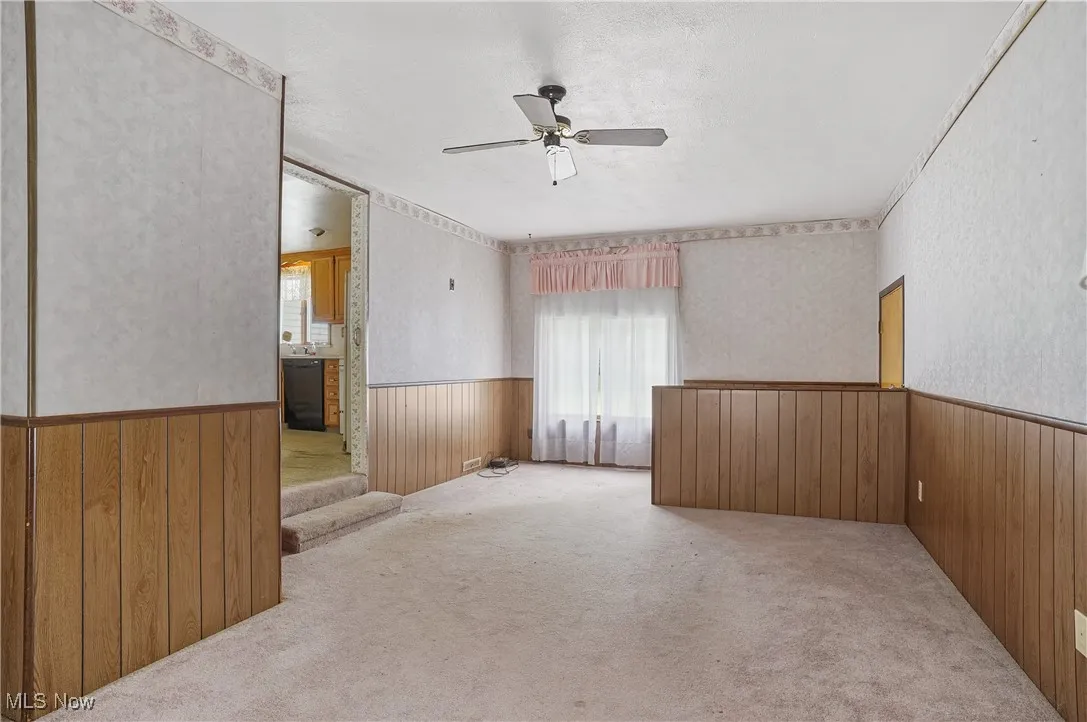 Unfurnished room with wooden walls, a wainscoted wall, carpet, a ceiling fan, and stairway
