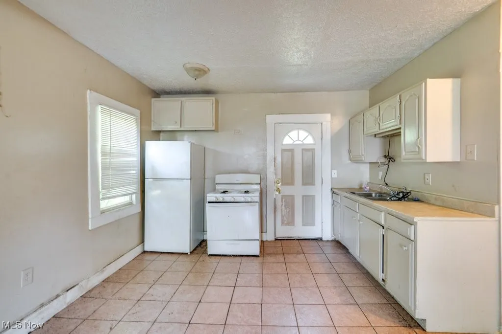 Kitchen featuring white appliances, a textured ceiling, light countertops, light tile patterned floors, and white cabinets
