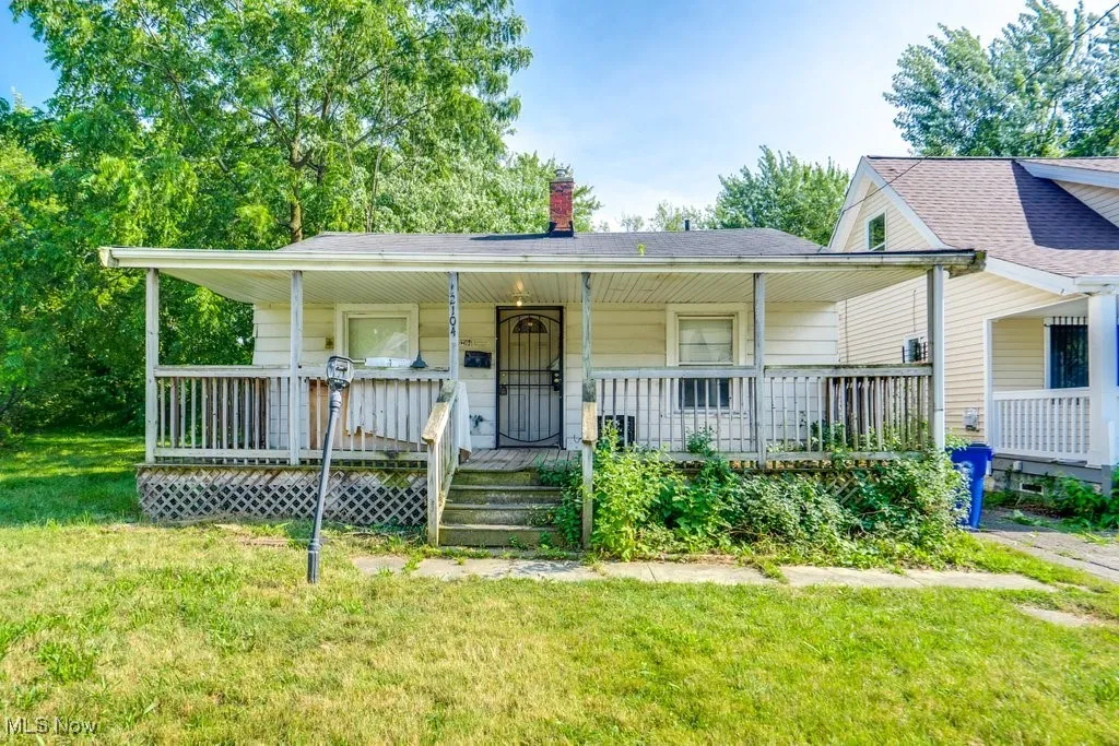 View of front of home with a chimney, covered porch, a front yard, and roof with shingles