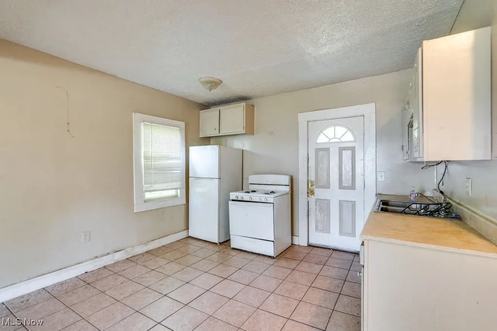 Kitchen with white appliances, light countertops, a textured ceiling, light tile patterned floors, and white cabinetry