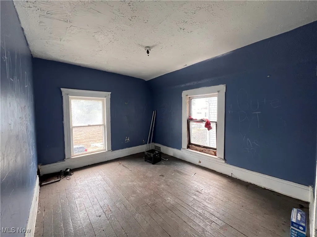 Unfurnished room featuring lofted ceiling, wood-type flooring, and a textured ceiling