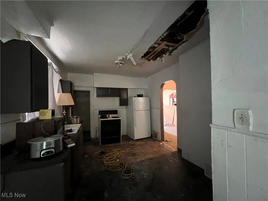 Kitchen featuring arched walkways, unfinished concrete flooring, freestanding refrigerator, and stove
