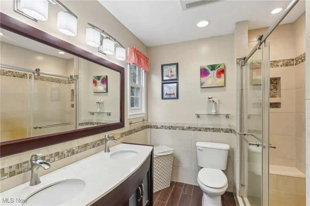 Primary bathroom with a double sink / vanity, special lighting, walk-in tile shower, commode and tile flooring