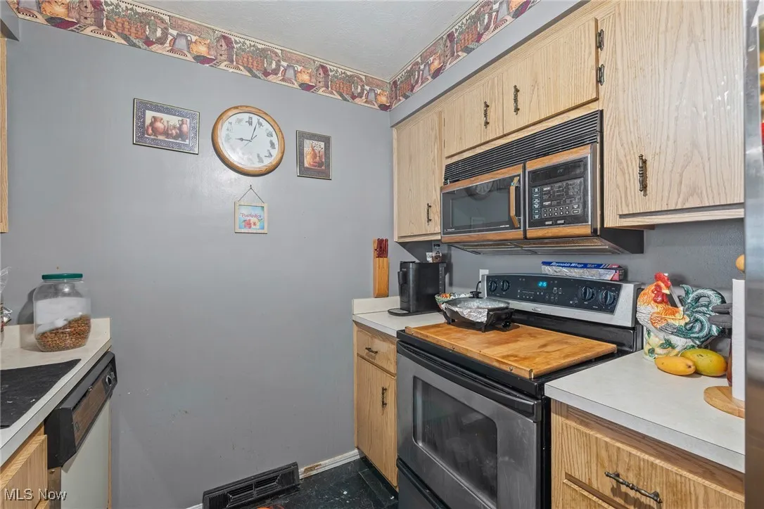 Kitchen featuring stainless steel range with electric stovetop, light countertops, white dishwasher, light brown cabinetry, and black microwave