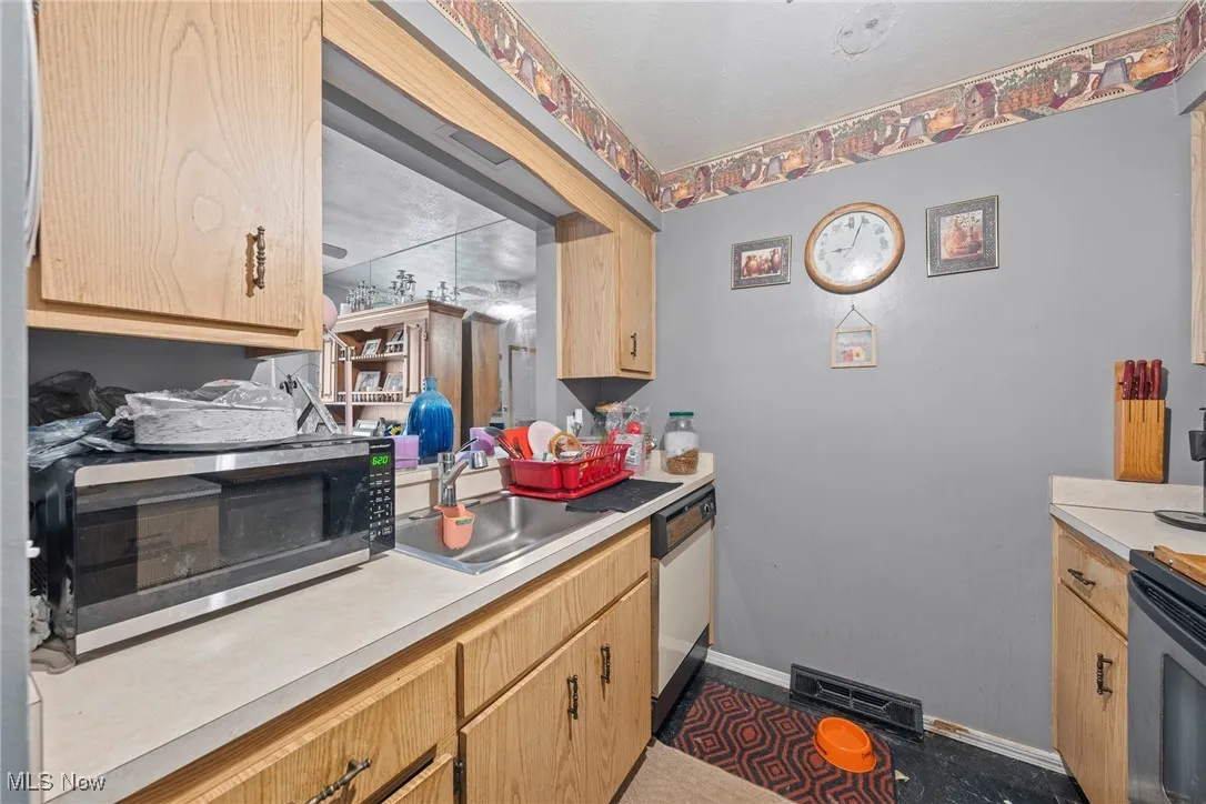 Kitchen with light countertops, stainless steel microwave, white dishwasher, and light brown cabinetry