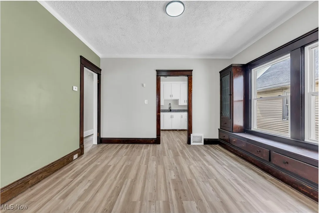 Spare room with a textured ceiling, light wood finished floors, and ornamental molding