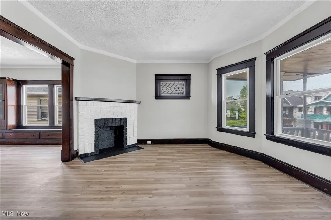 Unfurnished living room with light wood-type flooring, a textured ceiling, a fireplace, and ornamental molding
