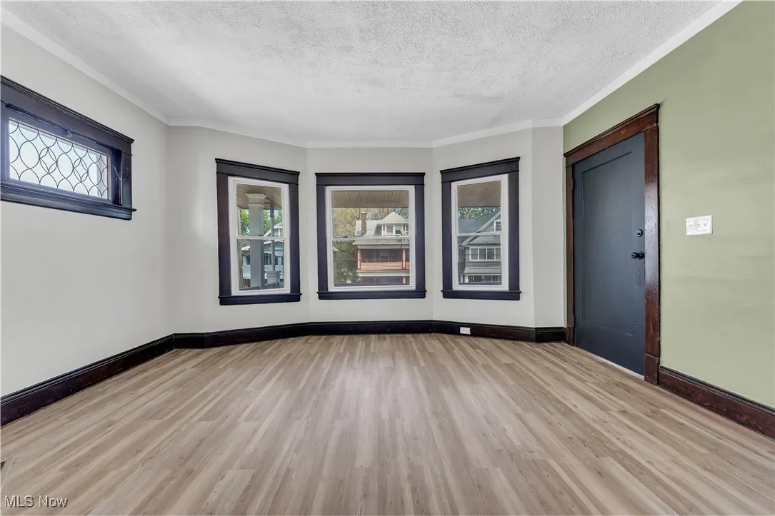 Empty room featuring wood finished floors, plenty of natural light, a textured ceiling, and crown molding