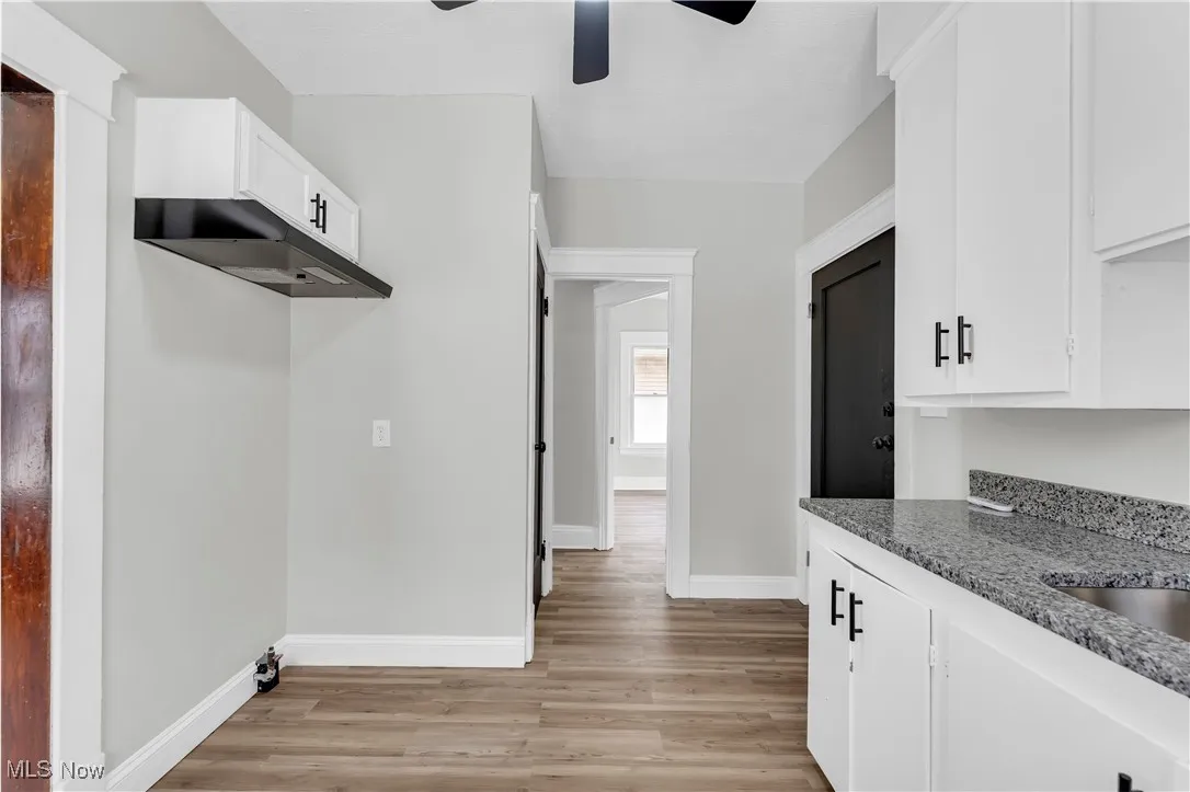 Kitchen featuring a ceiling fan, light wood-type flooring, white cabinets, under cabinet range hood, and light stone countertops