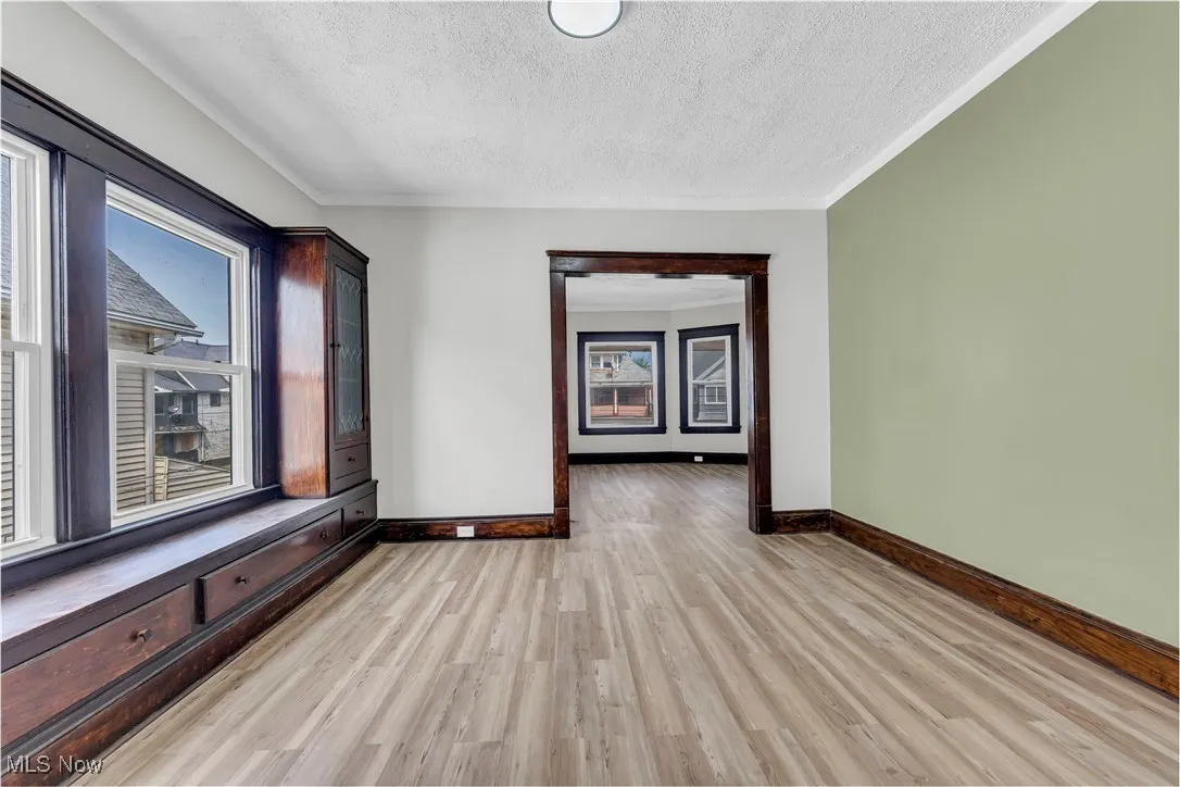Unfurnished room with a textured ceiling, plenty of natural light, light wood finished floors, and crown molding