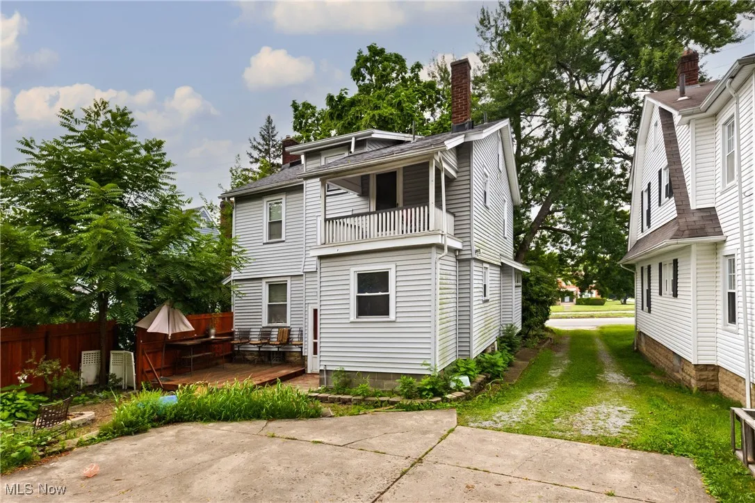 Back of property featuring a chimney, a balcony, a wooden deck, driveway, and a shingled roof