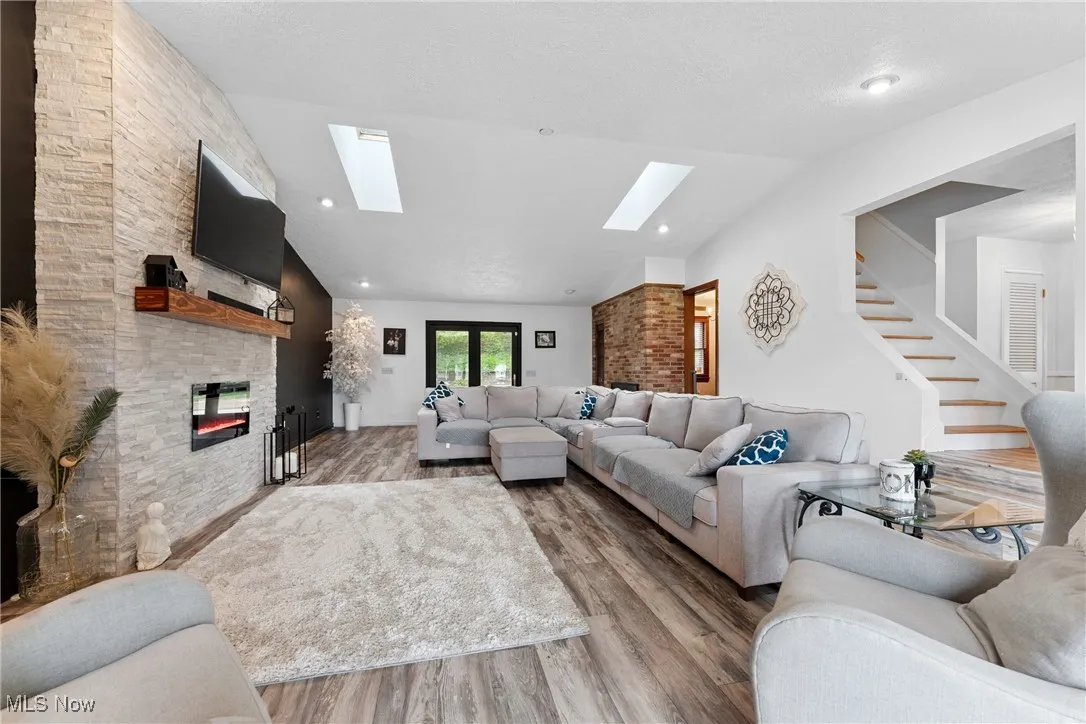 Living area with a skylight, vaulted ceiling, a stone fireplace, wood finished floors, and stairs