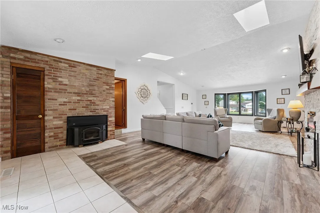 Living area featuring a skylight, light wood-style flooring, lofted ceiling, a wood stove, and a textured ceiling