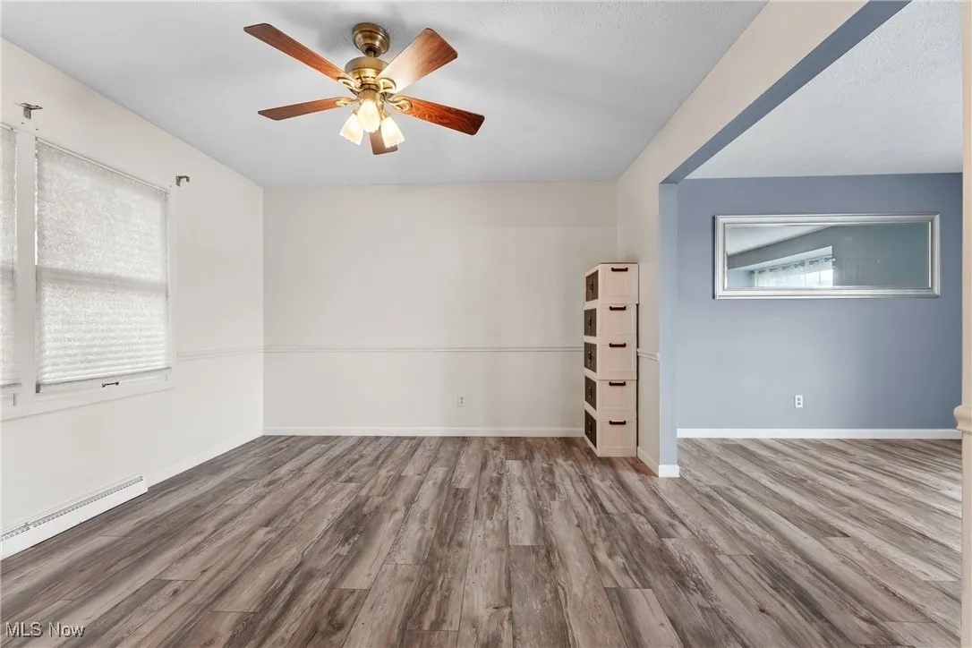 Spare room with wood finished floors, ceiling fan, and a baseboard radiator