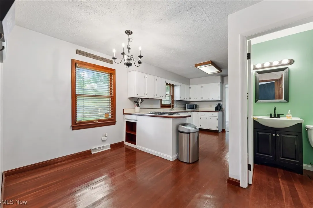 Kitchen featuring a chandelier, white cabinets, a peninsula, a textured ceiling, and dark wood-type flooring