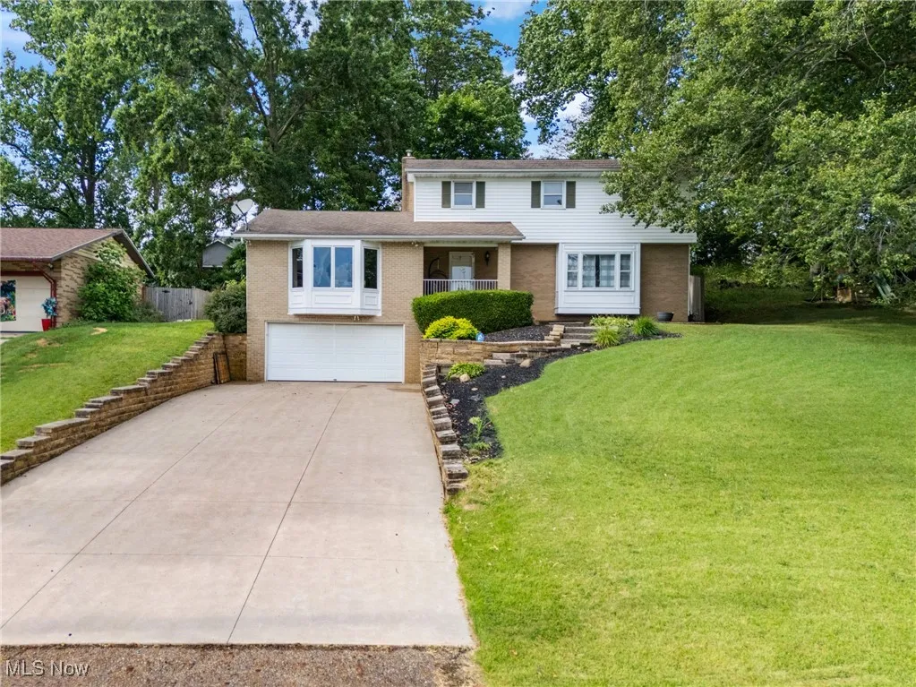 Traditional home with concrete driveway, brick siding, a garage, a front yard, and stairs