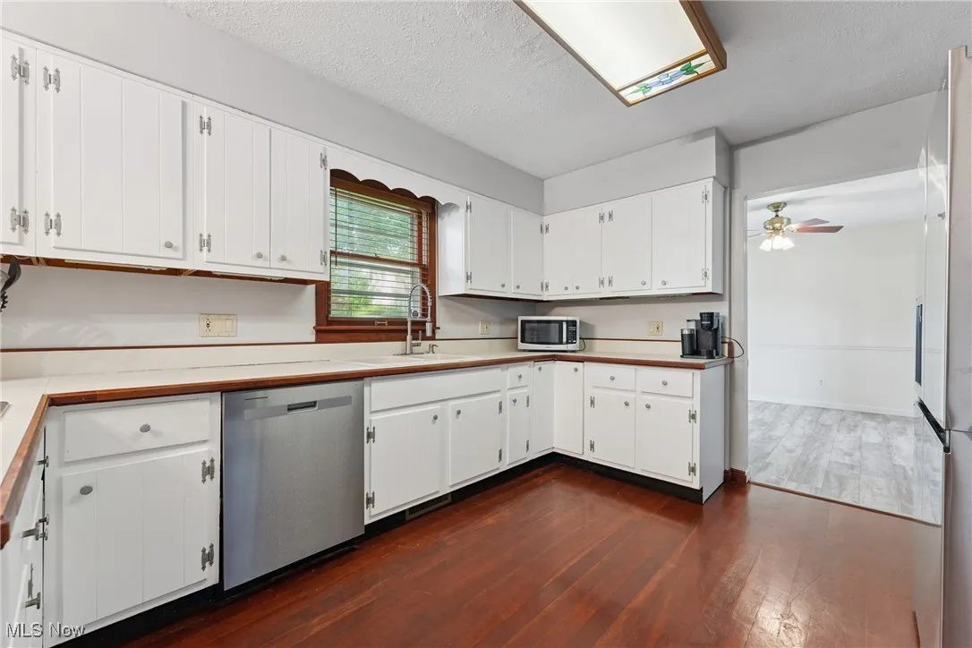 Kitchen with stainless steel appliances, dark wood-style floors, white cabinetry, a ceiling fan, and light countertops