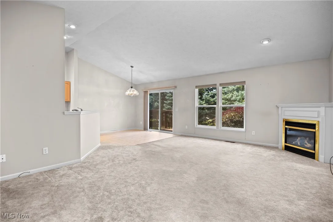 Unfurnished living room featuring carpet flooring, a chandelier, a glass covered fireplace, lofted ceiling, and recessed lighting