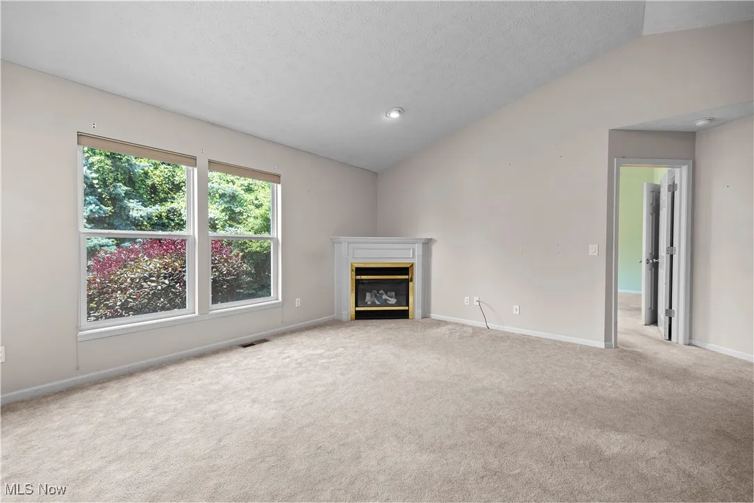 Unfurnished living room with lofted ceiling, carpet, a glass covered fireplace, and a textured ceiling