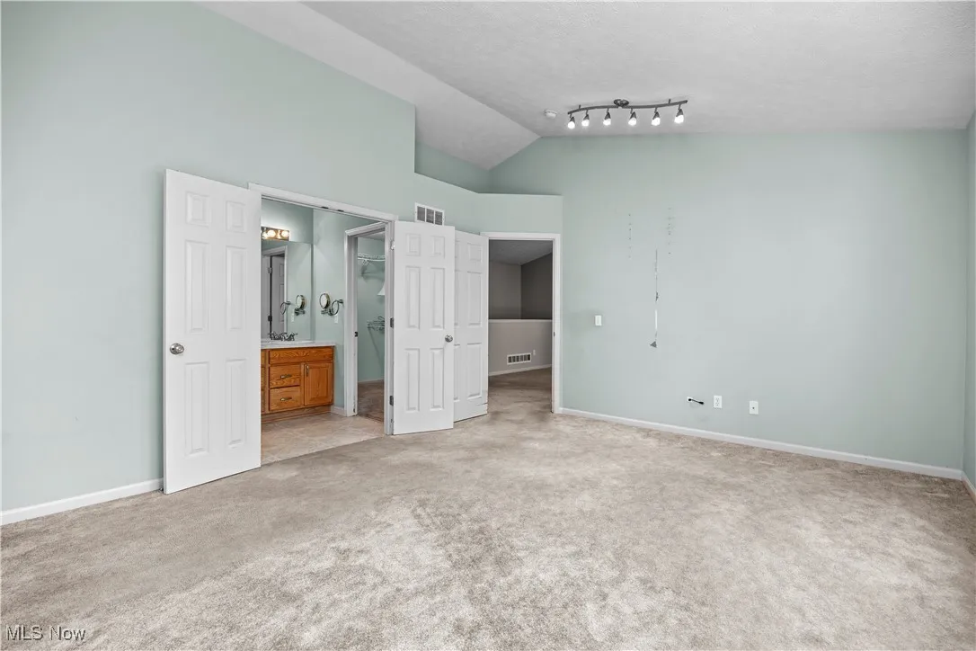 Unfurnished bedroom with light carpet, ensuite bath, high vaulted ceiling, and a textured ceiling