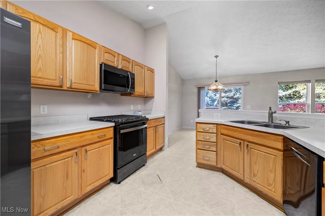 Kitchen with black appliances, plenty of natural light, light countertops, pendant lighting, and vaulted ceiling