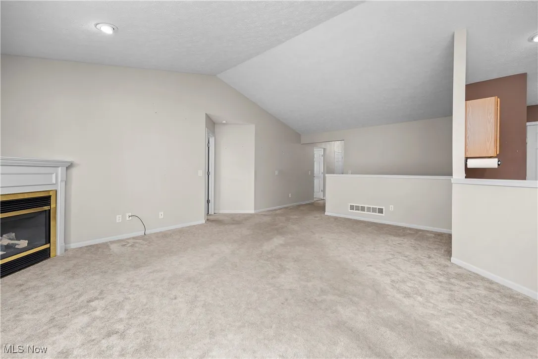Unfurnished living room with lofted ceiling, carpet floors, and a tiled fireplace