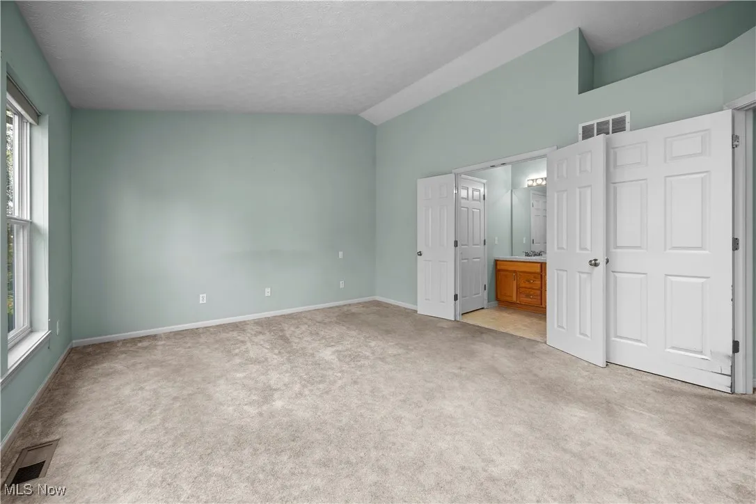 Unfurnished bedroom with light colored carpet, vaulted ceiling, ensuite bathroom, and a textured ceiling