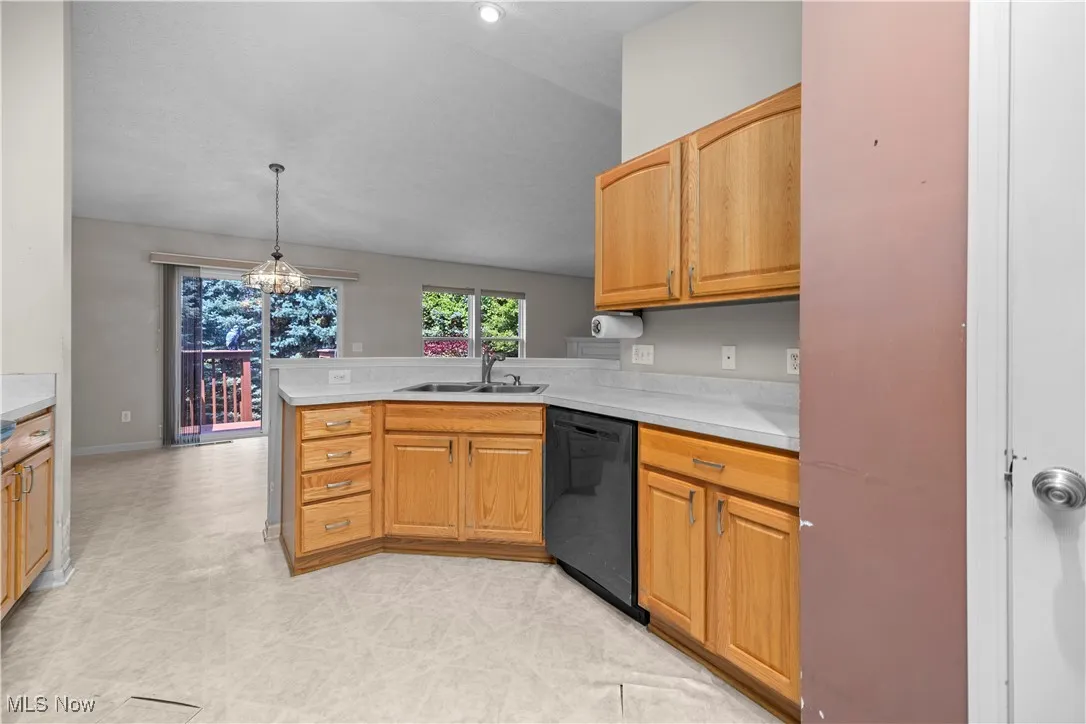 Kitchen with a peninsula, light countertops, black dishwasher, light floors, and pendant lighting