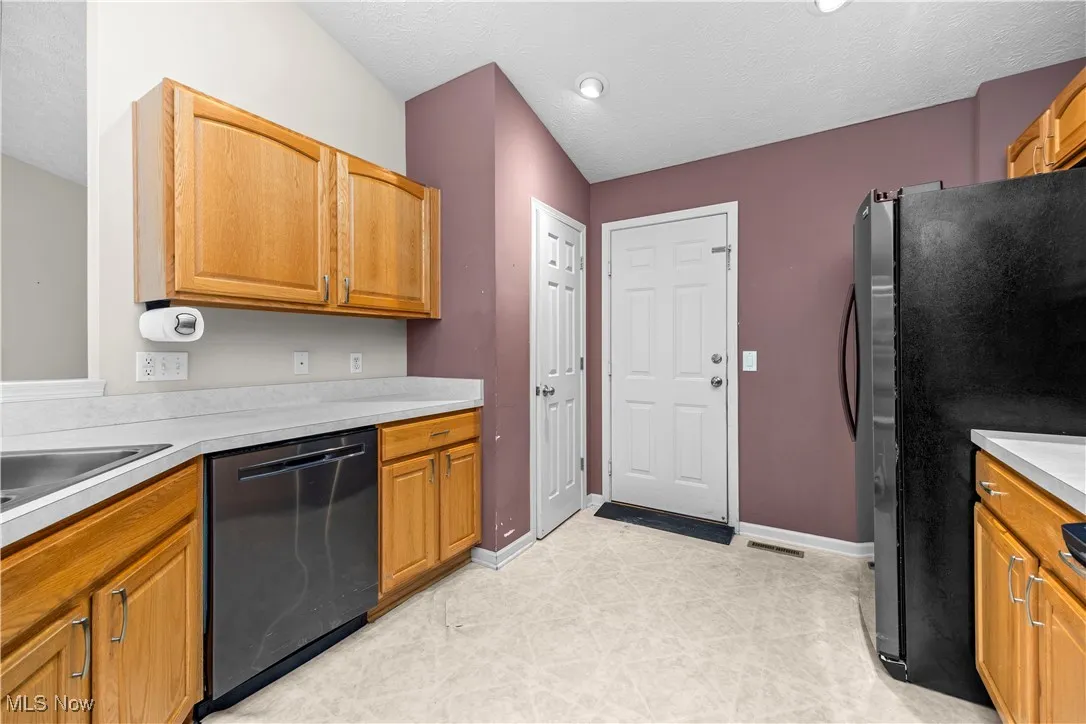 Kitchen featuring freestanding refrigerator, dishwashing machine, light countertops, and a textured ceiling