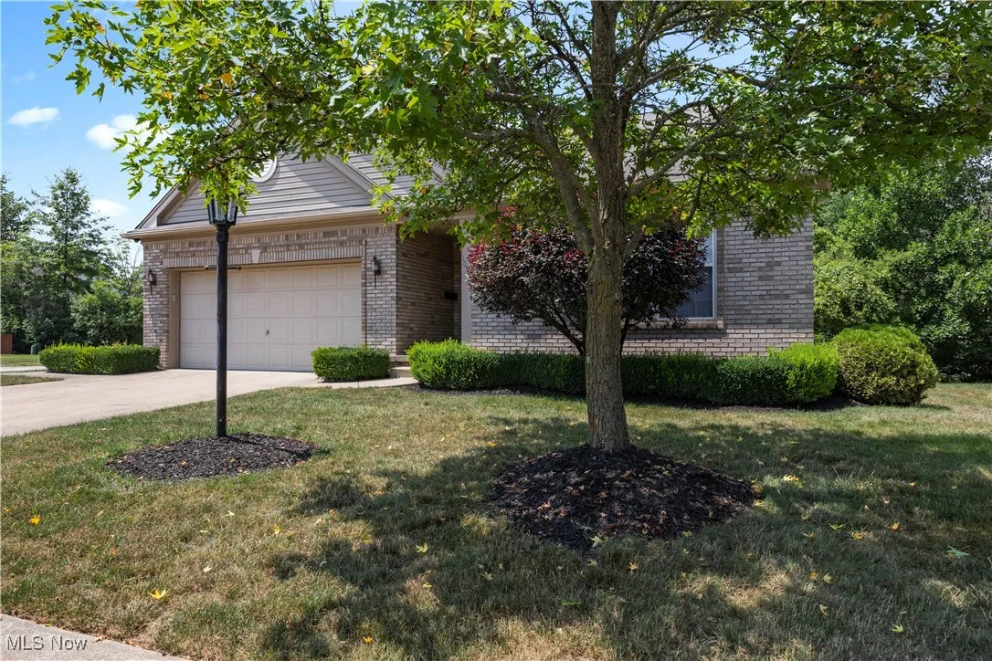 View of property hidden behind natural elements with brick siding, a garage, concrete driveway, and a front yard