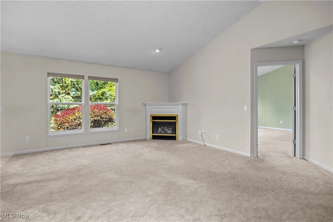 Unfurnished living room featuring carpet, lofted ceiling, and a glass covered fireplace