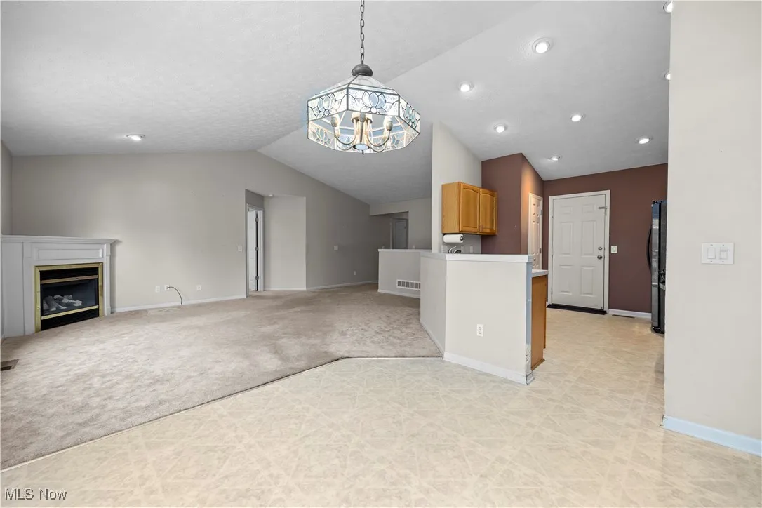 Kitchen with vaulted ceiling, open floor plan, light carpet, a glass covered fireplace, and black refrigerator