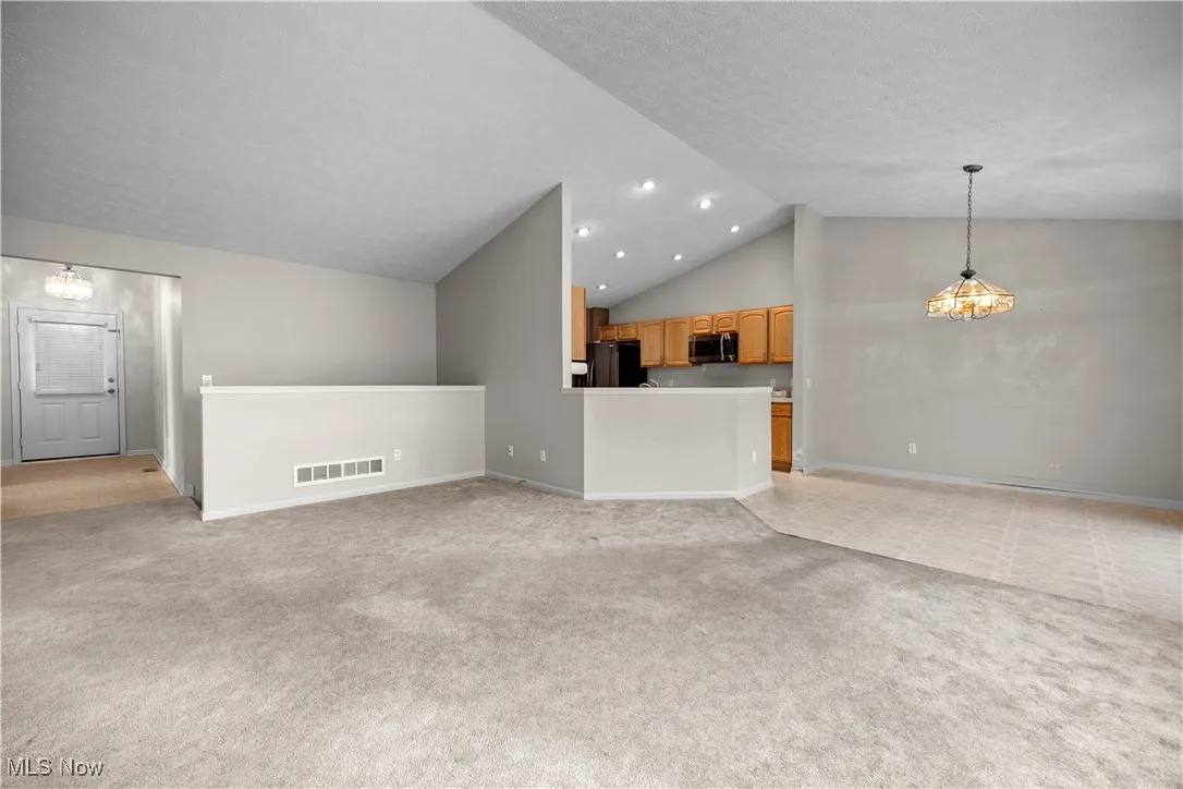 Unfurnished living room featuring vaulted ceiling, light carpet, and recessed lighting