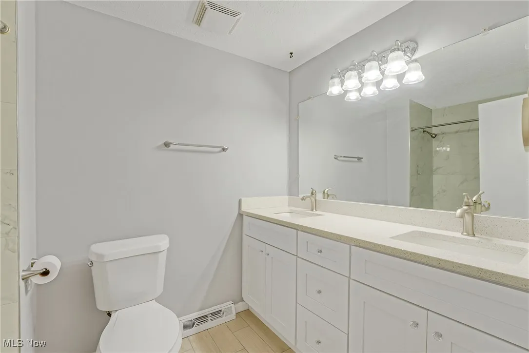 Primary ensuite bath with updated cabinets, quartz countertops, and a frameless glass door shower
