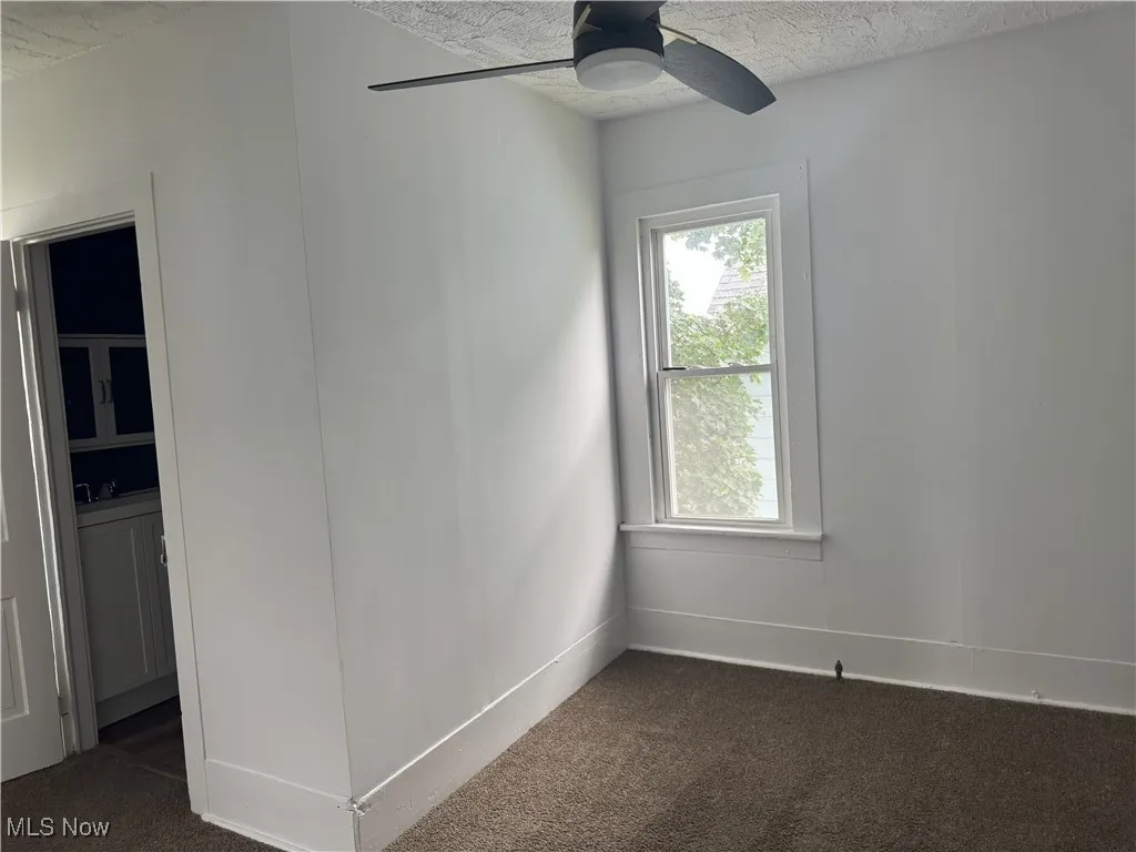 Unfurnished room featuring dark carpet, a ceiling fan, and a textured ceiling