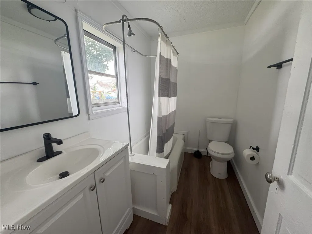 Bathroom featuring vanity, wood finished floors, shower / tub combo with curtain, and a textured ceiling