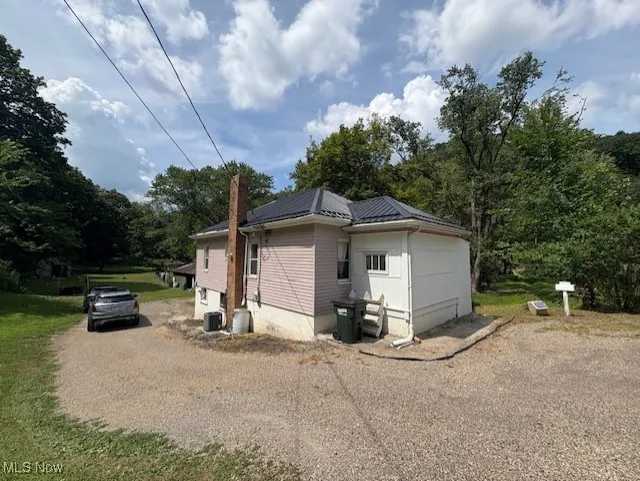 View of home's exterior featuring driveway, a chimney, and a metal roof