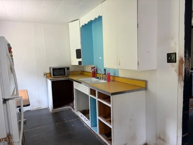 Kitchen featuring freestanding refrigerator, white cabinetry, and stainless steel microwave