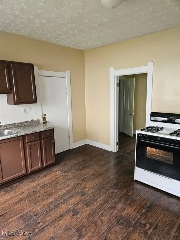 Kitchen with dark wood-style flooring, white gas stove, a textured ceiling, and dark brown cabinets