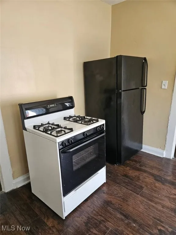 Kitchen featuring white gas stove, dark wood finished floors, and freestanding refrigerator