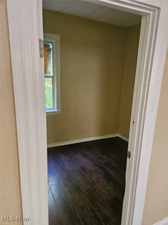 Spare room with dark wood-type flooring and baseboards