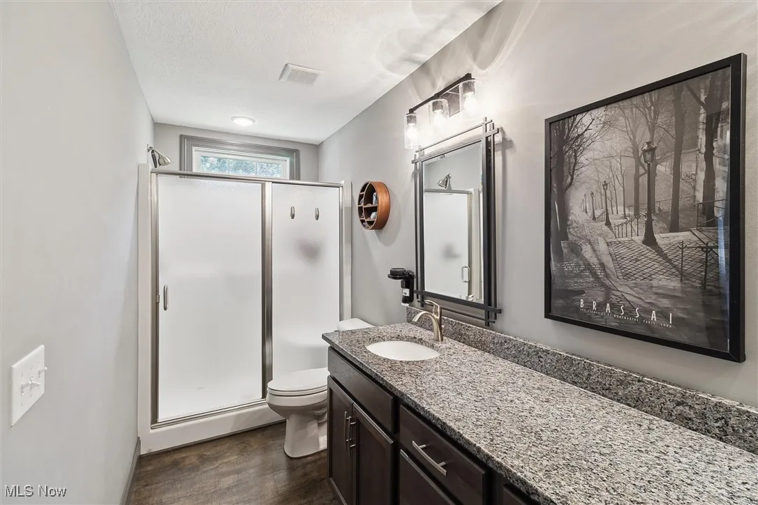Full bathroom with wood finished floors, vanity, a stall shower, and a textured ceiling