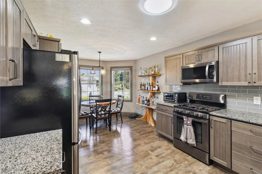 Kitchen featuring appliances with stainless steel finishes, a textured ceiling, decorative backsplash, light stone counters, and light wood finished floors